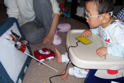 toddler in low highchair wearing prescription googles and using a screen and touchpad